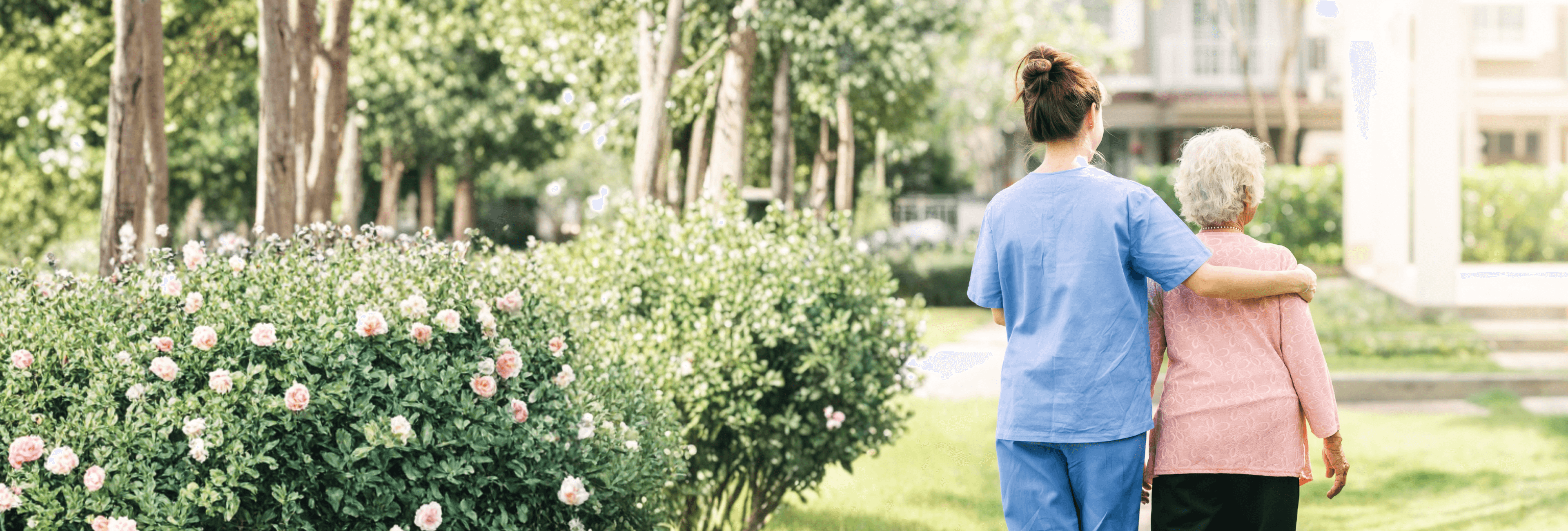 A caregiver walking with an elderly person through a garden